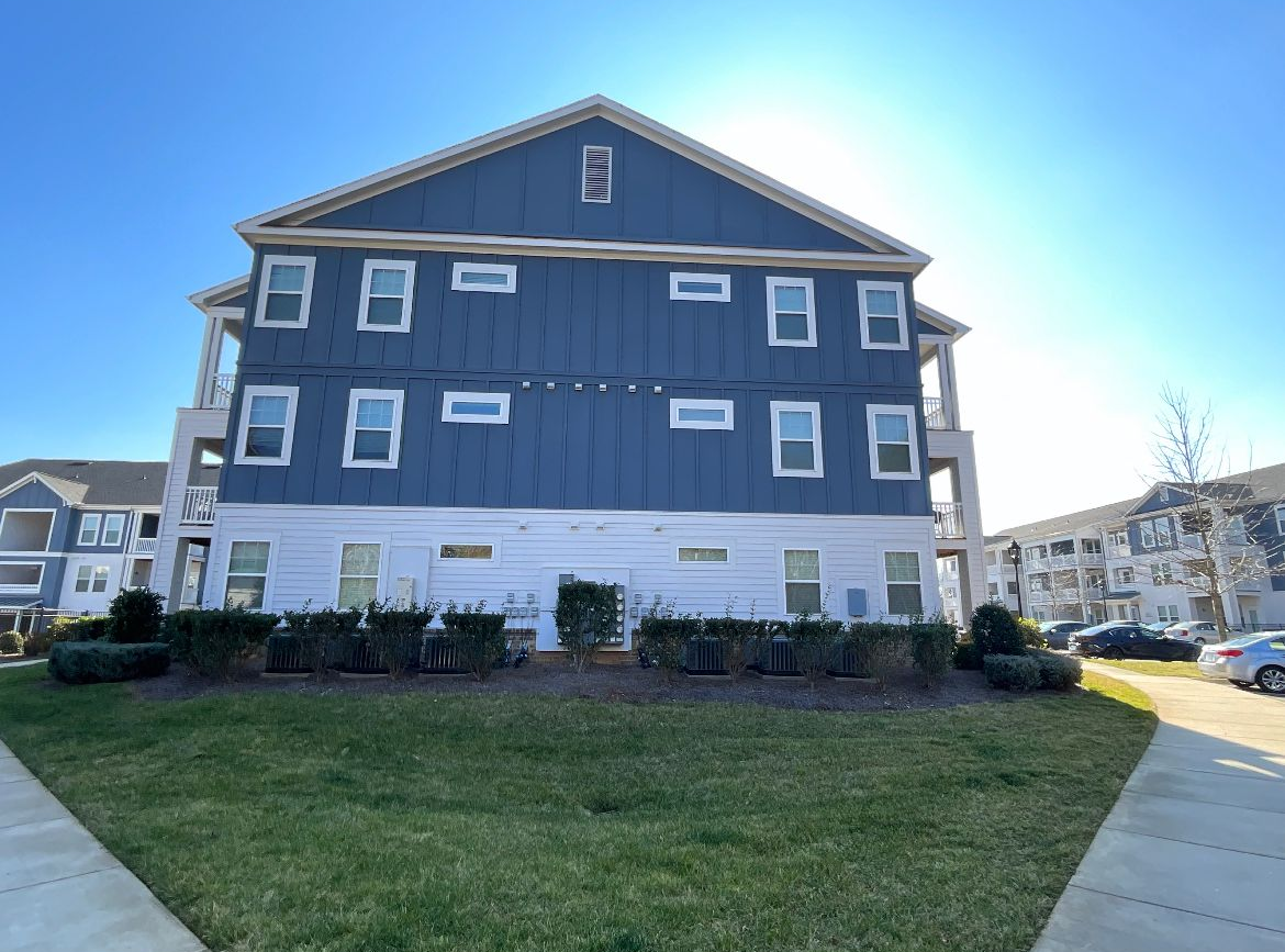 Three-story blue and white apartment building with a sunny sky and green lawn.