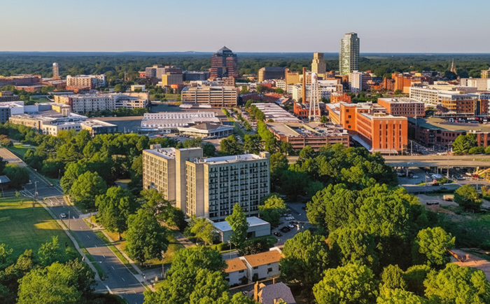 Aerial view of a city skyline with buildings and trees under a clear, blue sky.