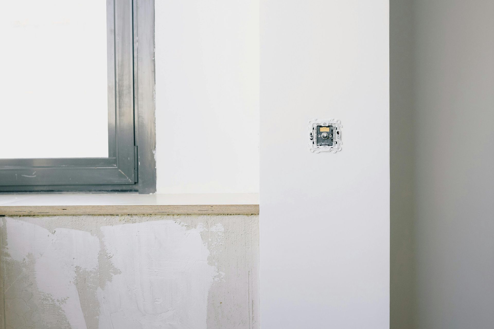 Interior wall under construction with a window and exposed electrical outlet.