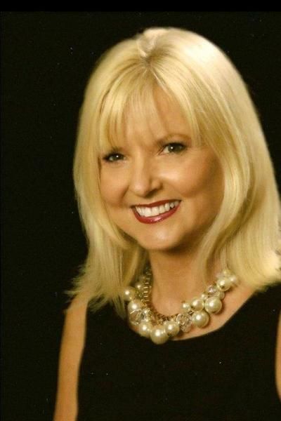 women in black dress A woman with blonde hair and a pearl necklace smiles for the camera