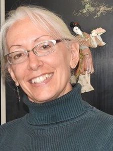 women in turtleneck sweater with glasses A woman wearing glasses and a turtleneck is smiling in front of a painting