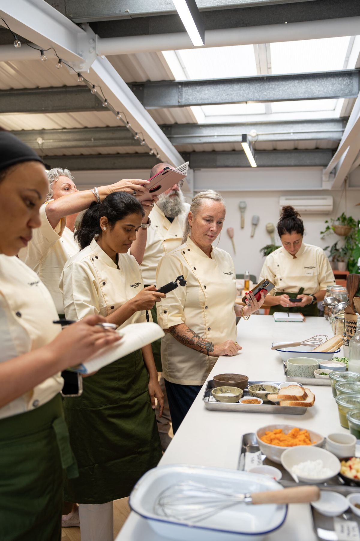 Academy students in chef whites filming and taking notes during a cooking demonstration, Bettina’s Kitchen by REGO Creative