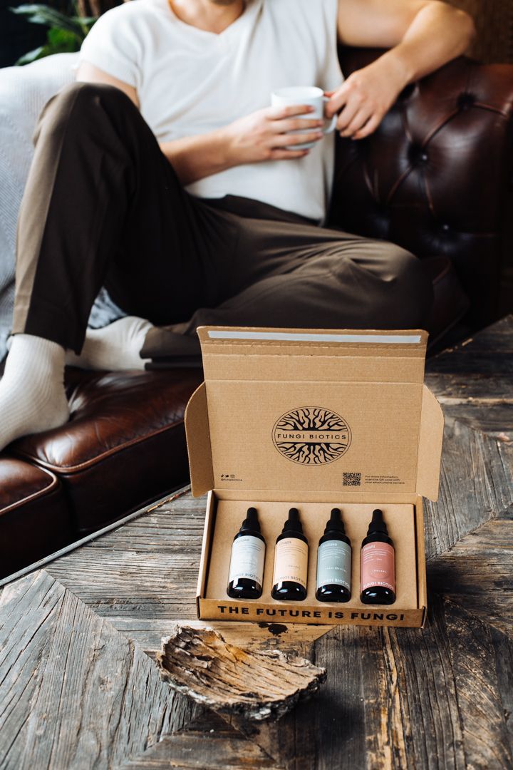 Open Fungi Biotics gift box of four tincture bottles with the words The Future Is Fungi, in front of a man relaxing on a leather sofa with a cup, by REGO Creative