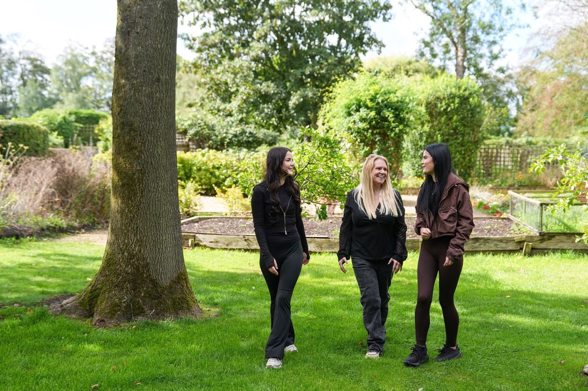 Three women walking and chatting on a lawn in a garden beside a large tree, Lancashire County Council by REGO Creative