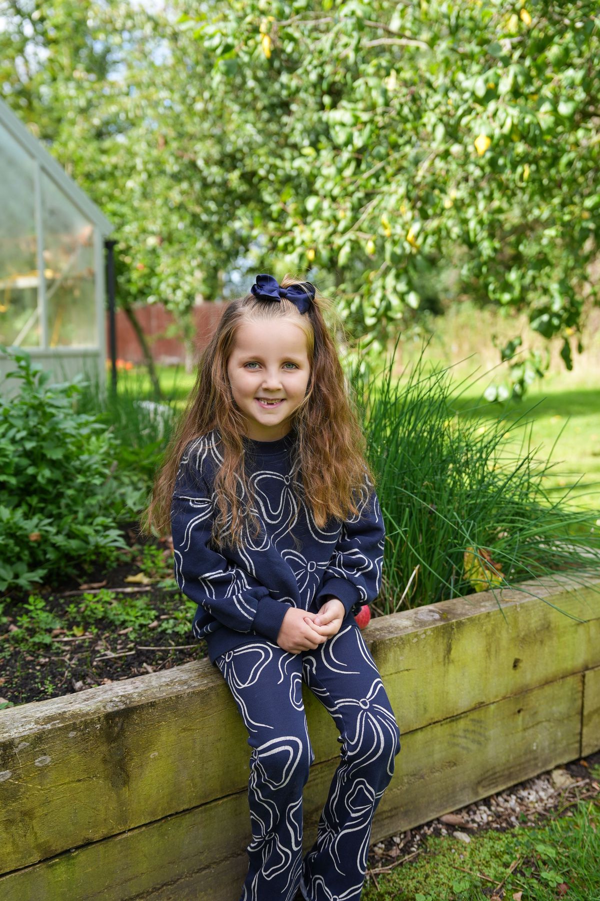 Smiling young girl with a navy bow sitting on a raised garden bed, Lancashire County Council by REGO Creative