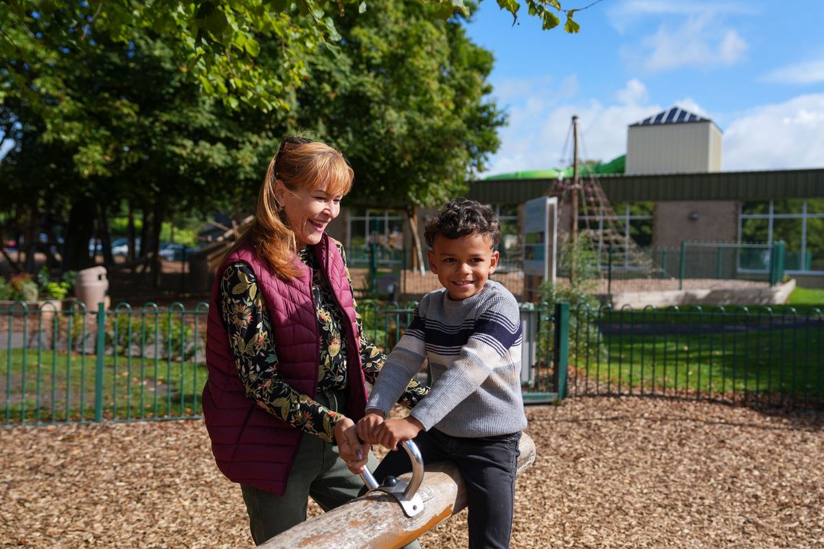 Foster carer smiling beside a young boy on a playground seesaw, Lancashire County Council by REGO Creative