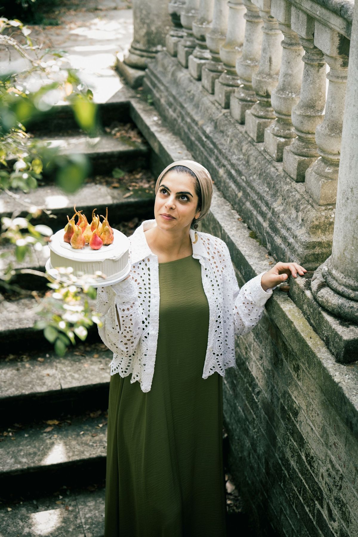 Nour, founder of Nuun Cakes London, holding a pear cake on a stone staircase, by REGO Creative