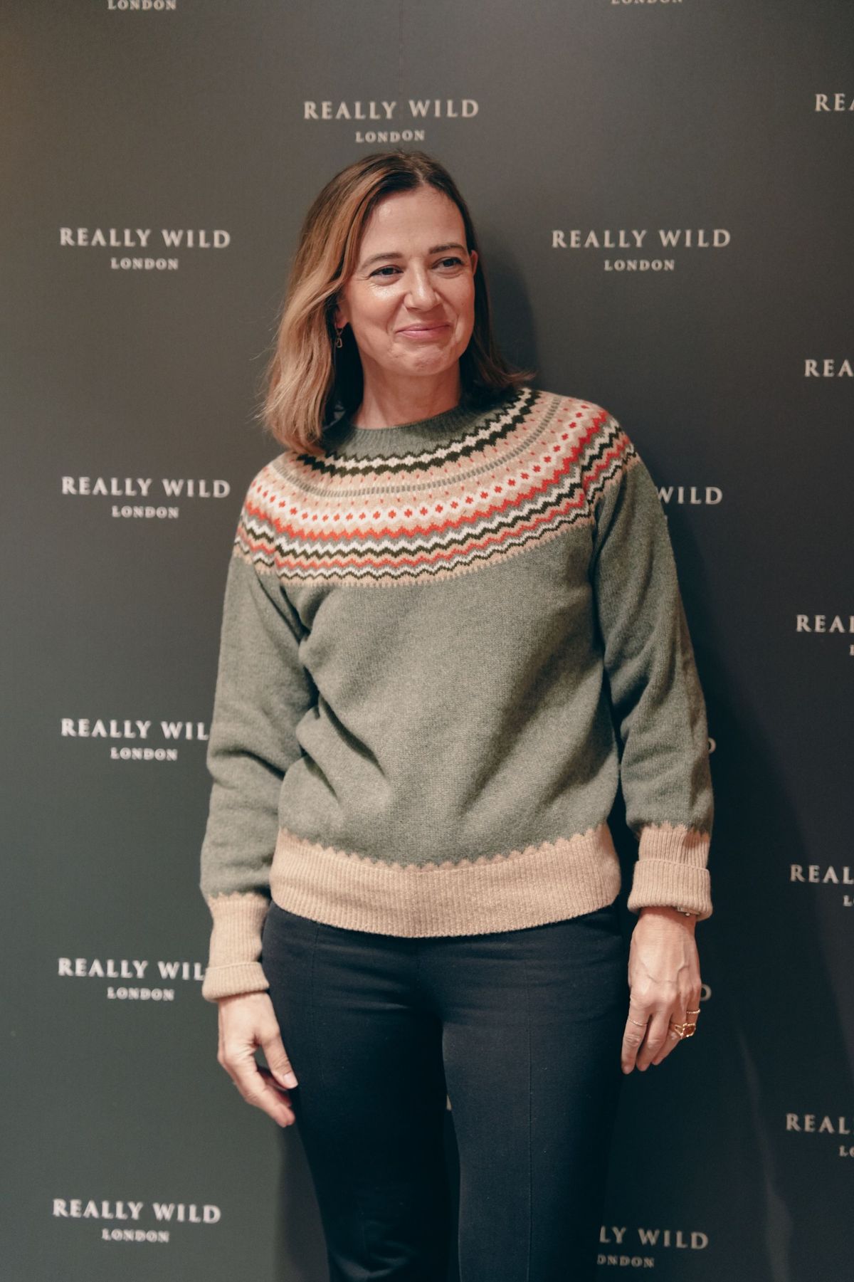 Guest smiling in front of the Really Wild London backdrop wearing a Fair Isle jumper, by REGO Creative
