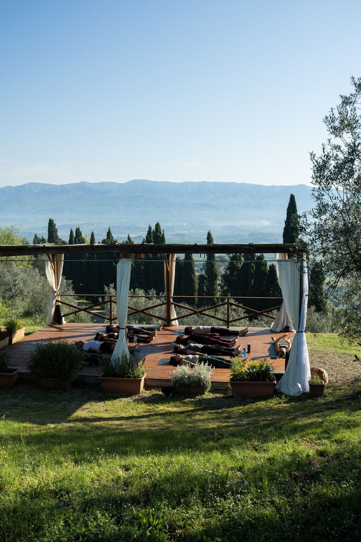 Guests resting in savasana on the deck with cypress trees and mountains beyond, Tuscan Fitness by REGO Creative