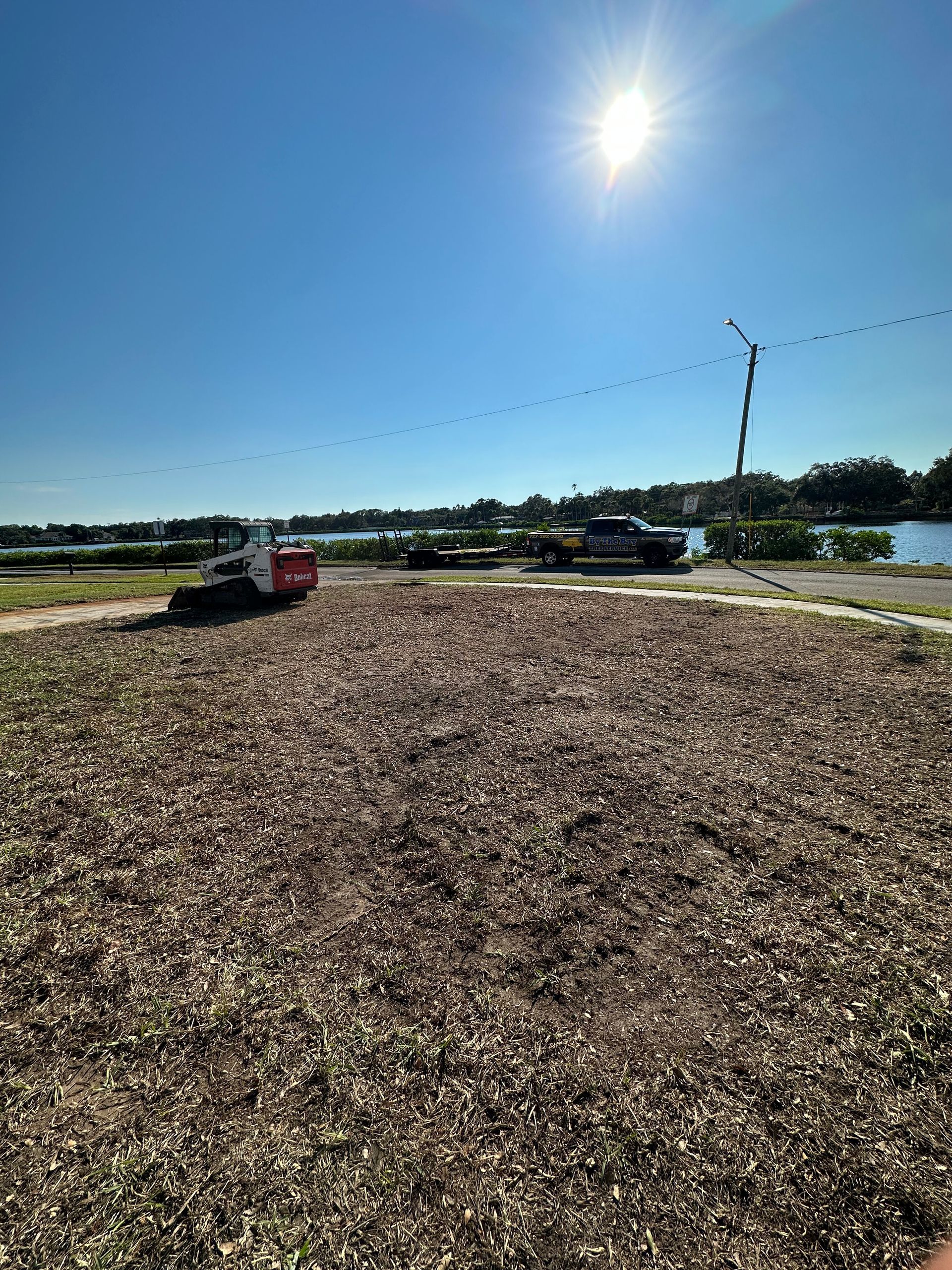 Bright sunny day over a large gravel lot with vehicles, fencing, and distant trees under a clear blue sky