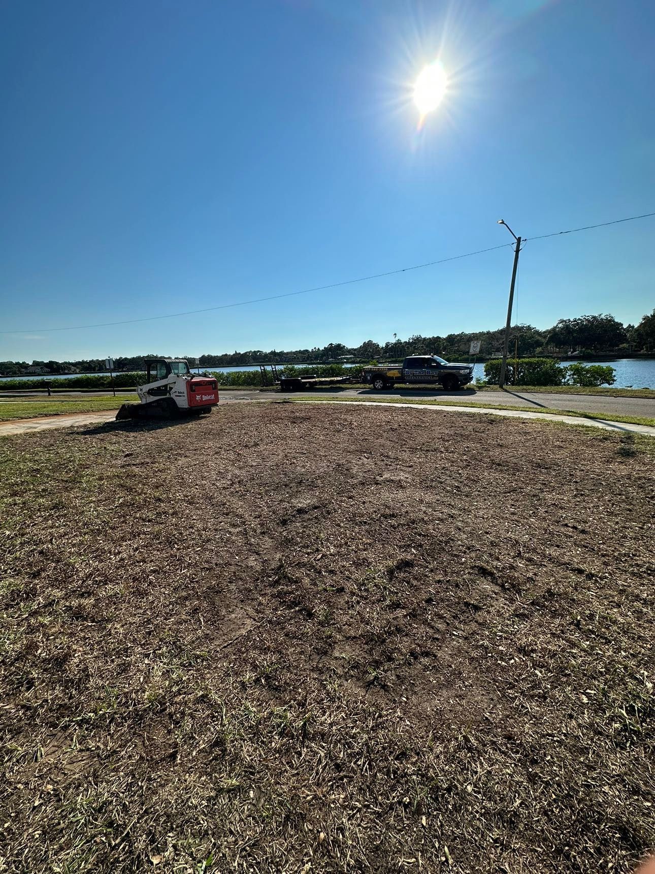 Sunny outdoor lot with two parked vehicles, a gravel foreground, and a pond in the distance