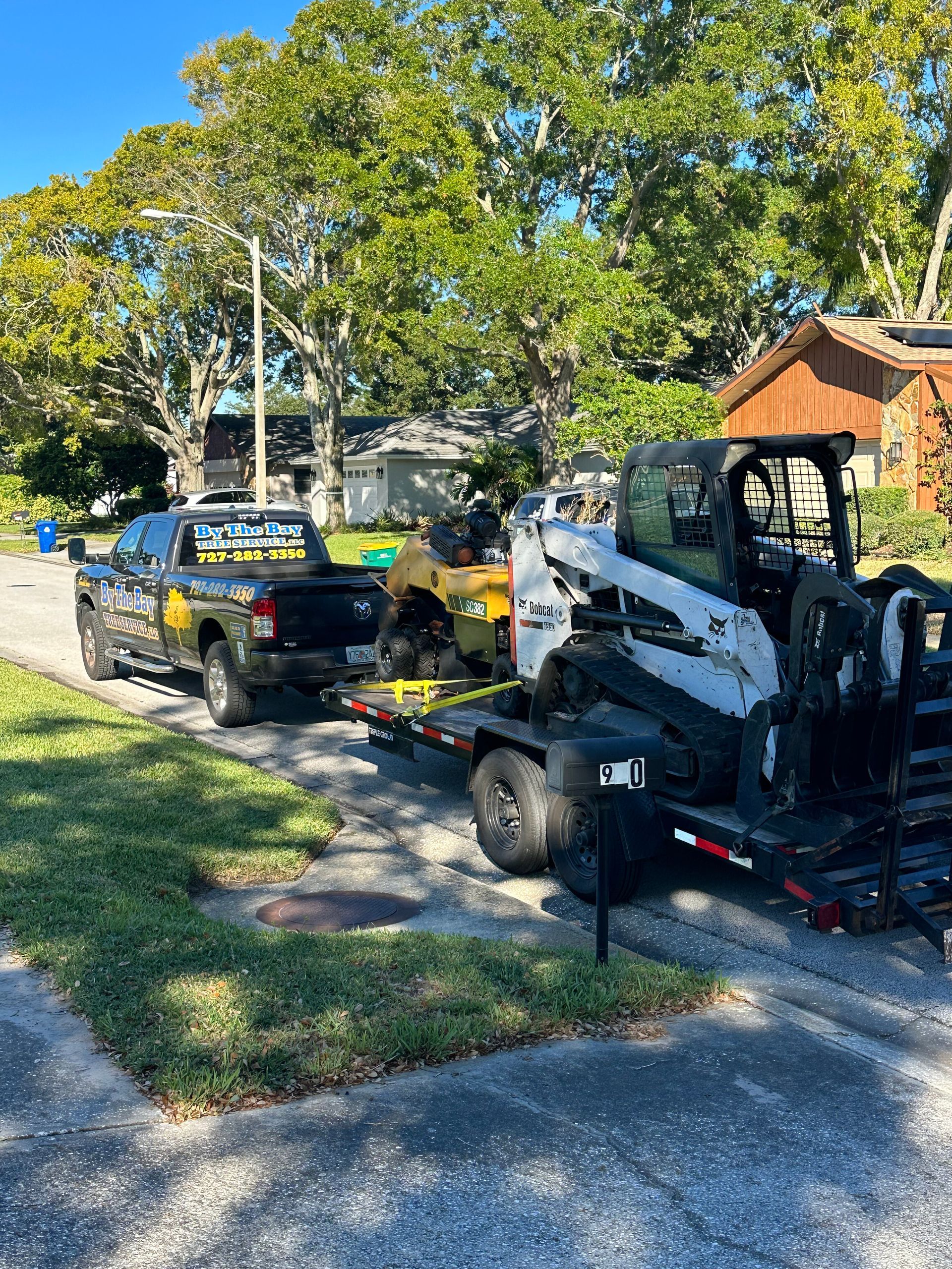 Two landscaping trucks with trailer-mounted equipment parked along a tree-lined residential street.
