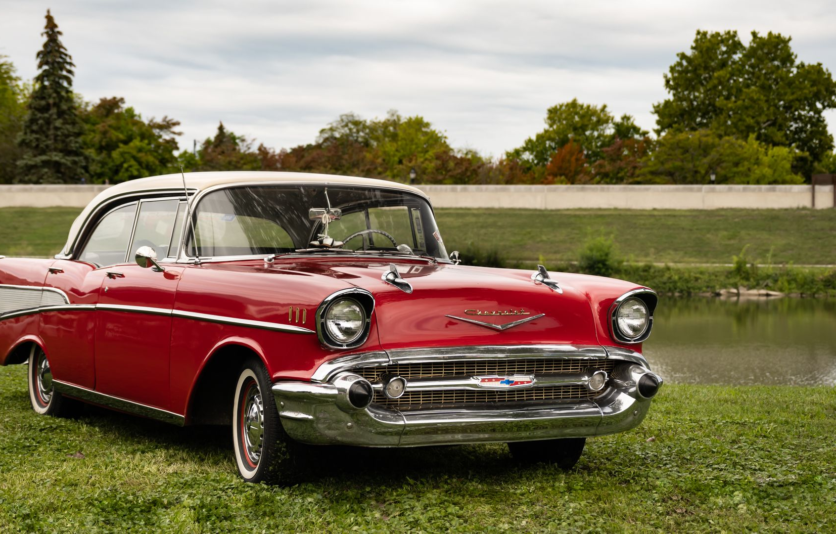 A classic red and white 1957 Chevrolet Bel Air parked on a grassy riverbank.