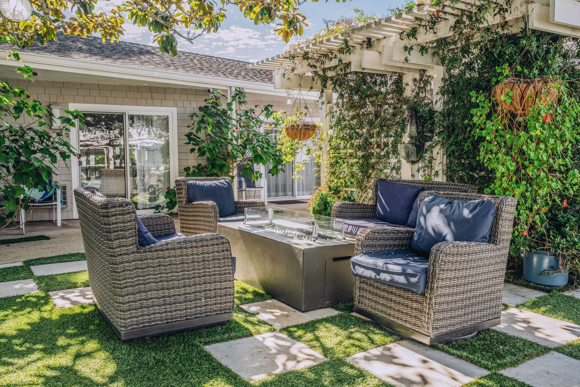 Outdoor patio seating with wicker chairs, a bench, and a table under a shaded pergola in a garden courtyard