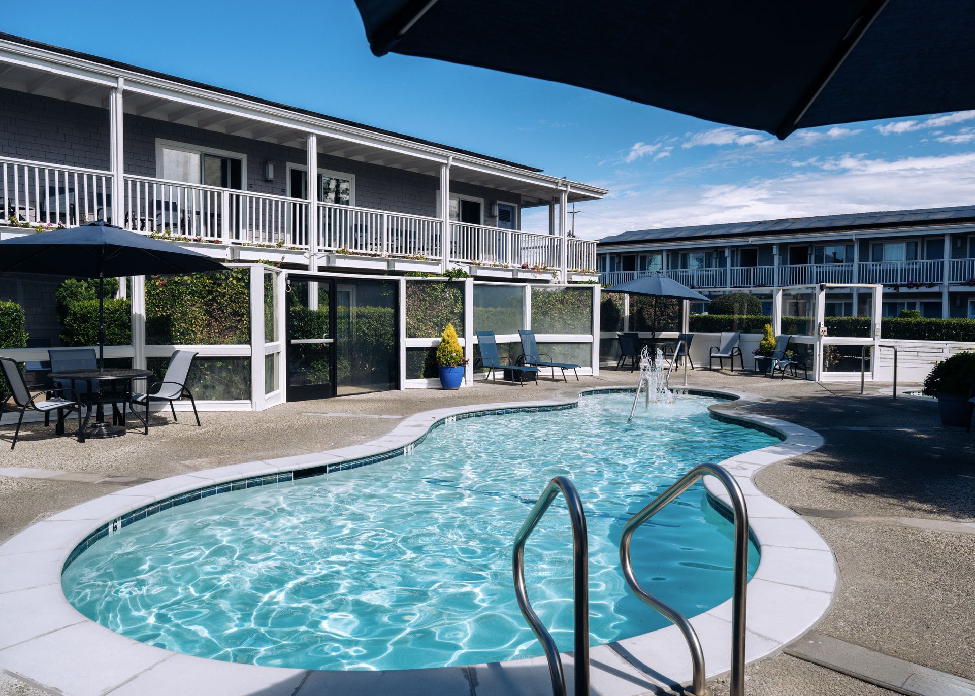 Courtyard motel with a round blue pool, white railings, and lounge chairs under a clear sky