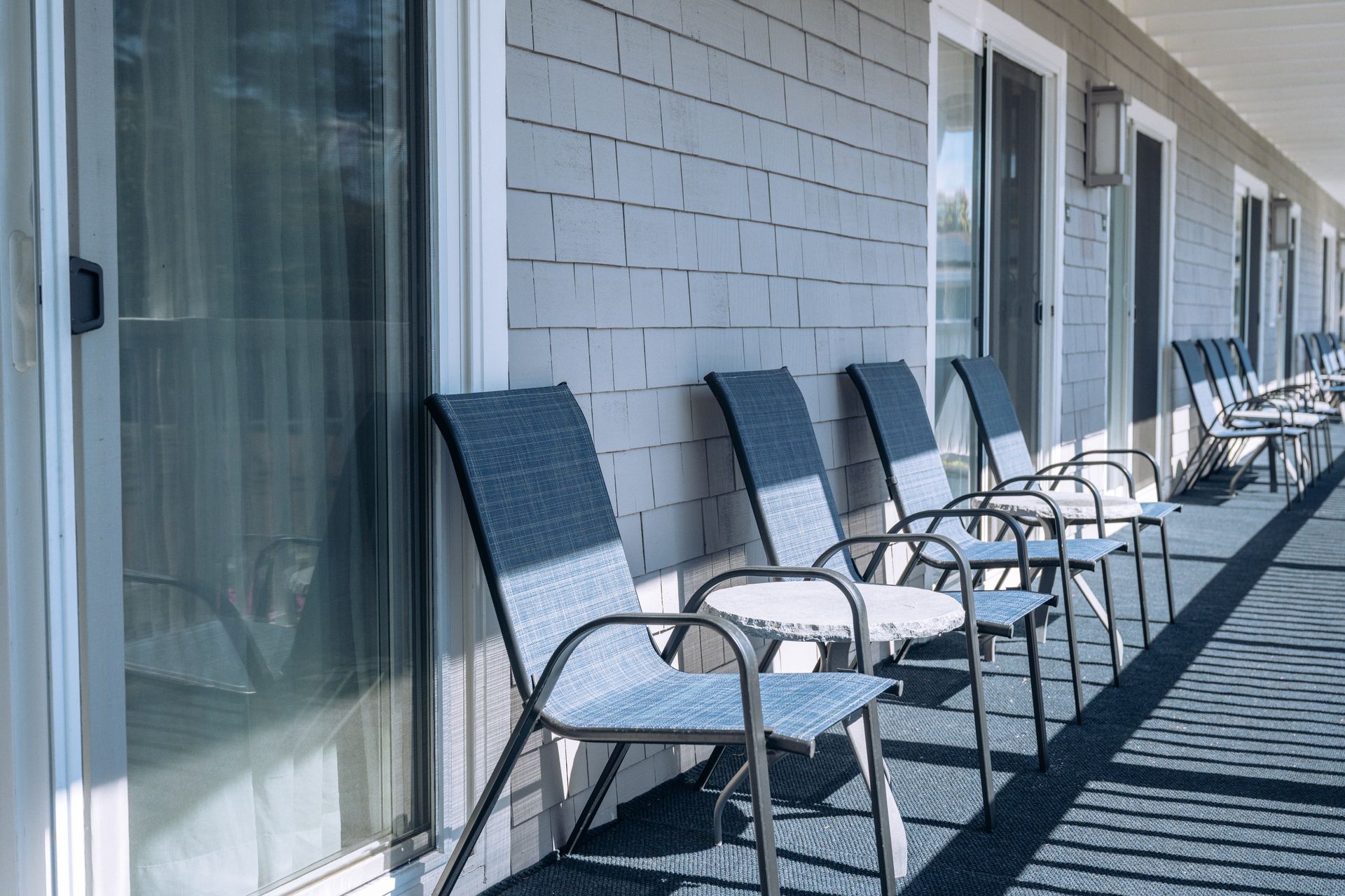 White motel-style balcony with blue chairs and sliding glass doors in bright sunlight
