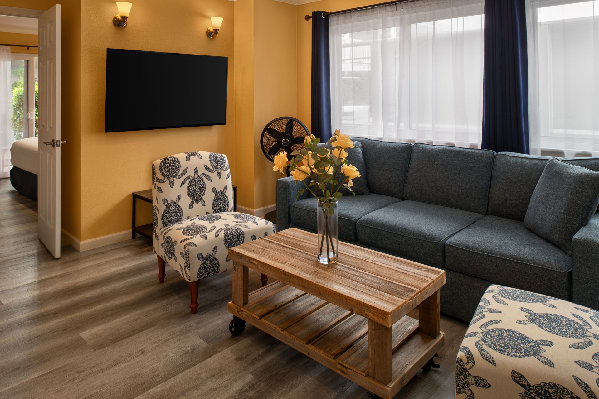Cozy living room with dark sofa, patterned chairs, coffee table, wall-mounted TV, and window with curtains