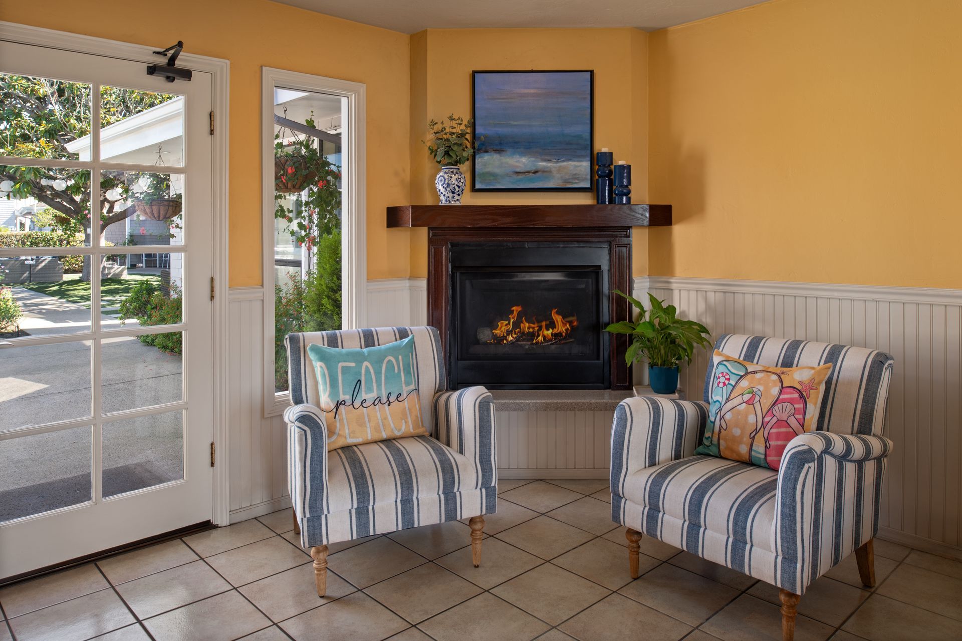 Cozy living room with striped chairs, fireplace, ocean painting, and a glass door to the outside