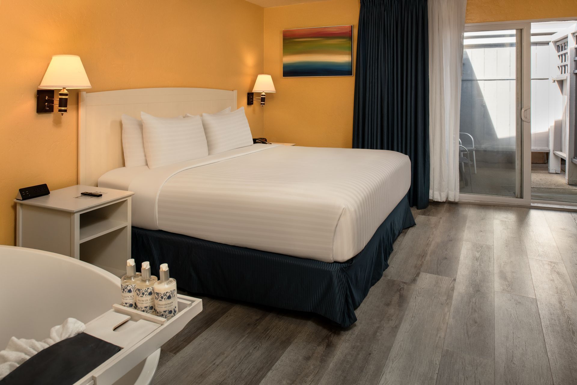 Hotel room with two white beds, warm wall lamps, and a balcony door with curtains.