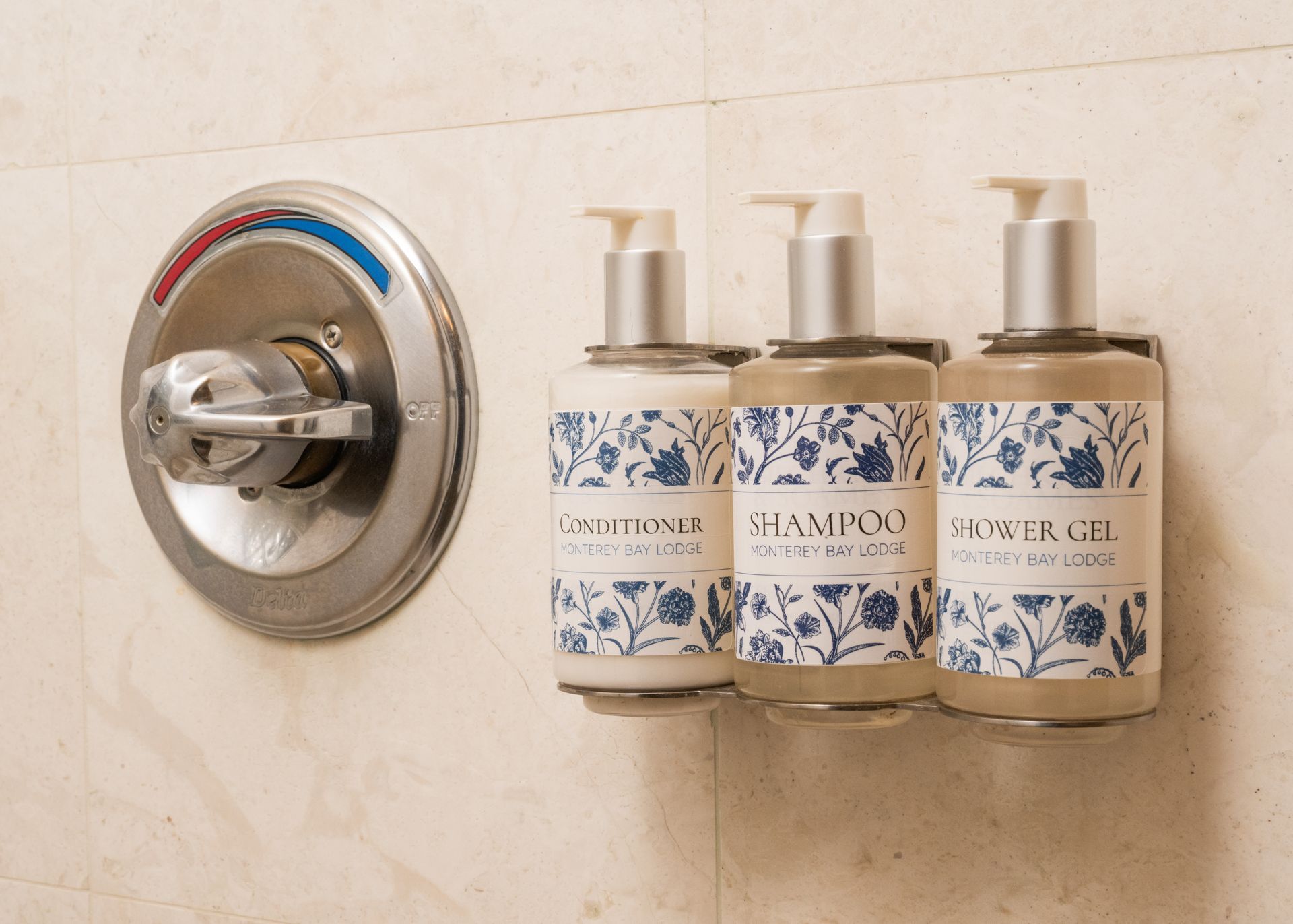 Shower wall with chrome control and three hanging soap dispensers on beige tile.