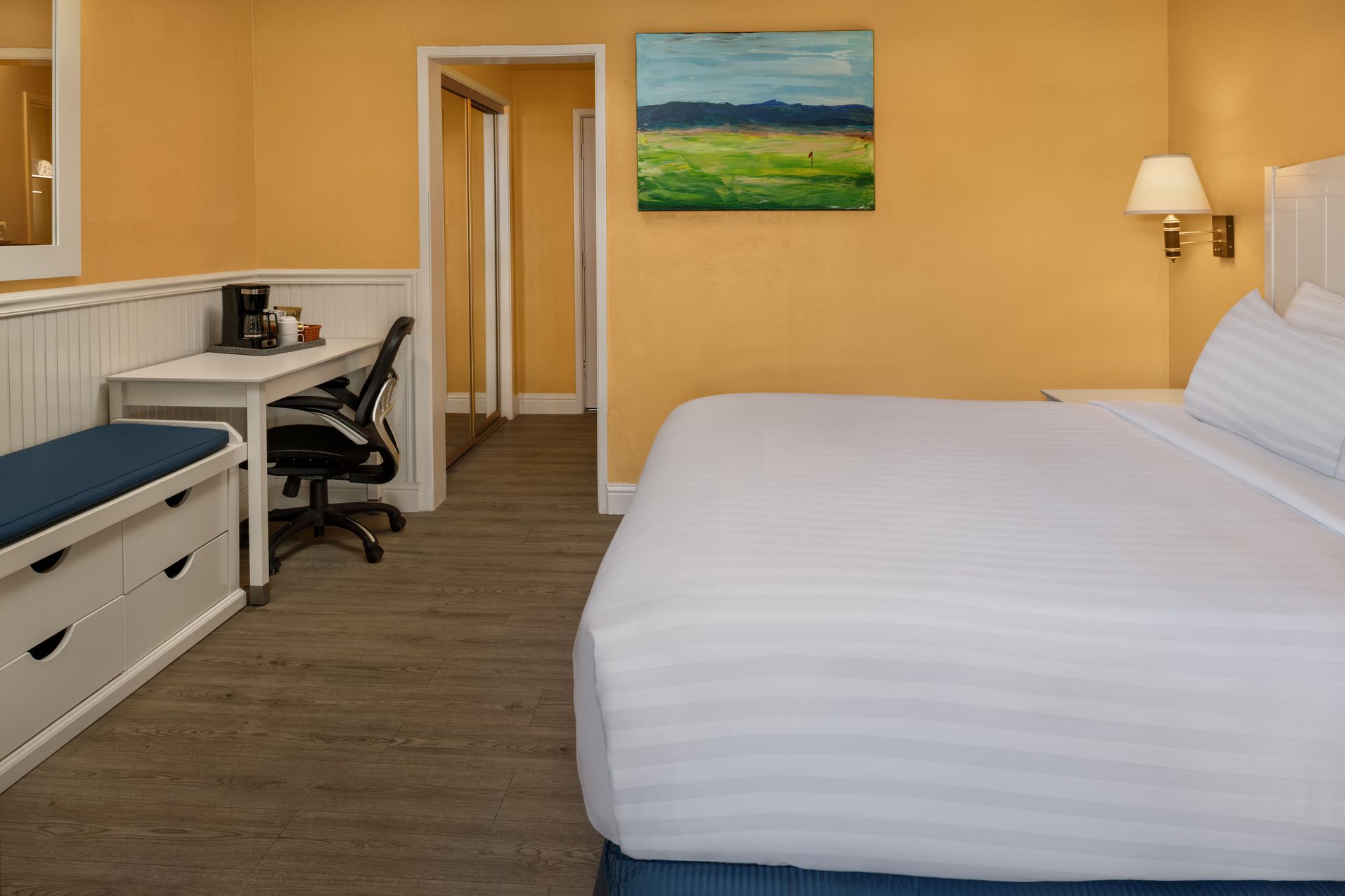 Modern hotel room with a neatly made bed, desk, chair, and wall art.