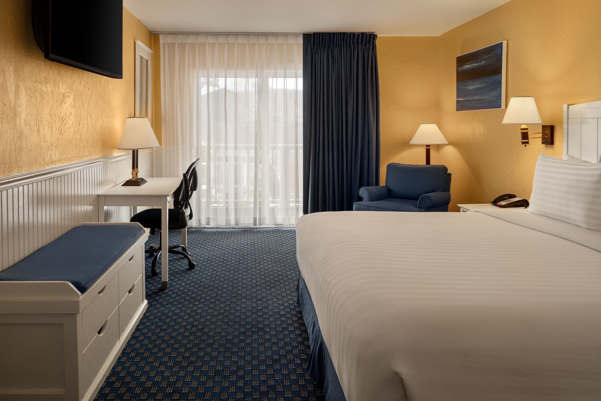 Hotel room with two beds, blue chair, desk, and window with curtains.