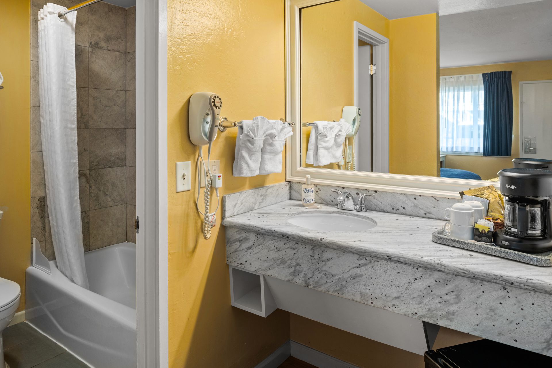 Hotel bathroom with shower, marble sink, mirror, and yellow walls