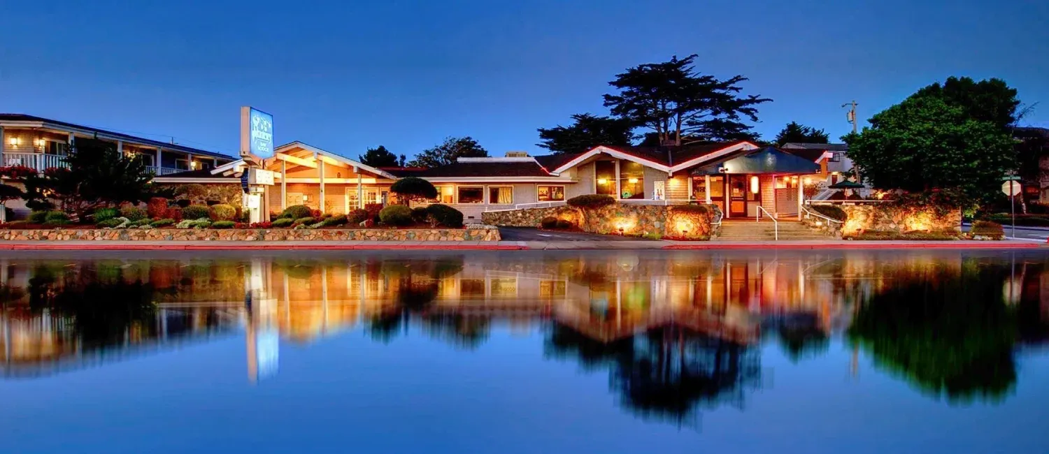 Lit waterfront buildings at dusk reflecting on calm water, with a blue sky overhead