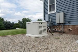 Residential backup generator beside a blue house on a gravel bed