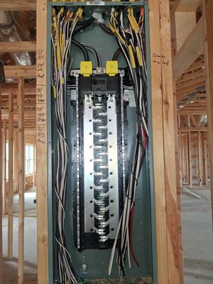 Electrical breaker panel in a framed wall, with exposed wiring in a construction site.
