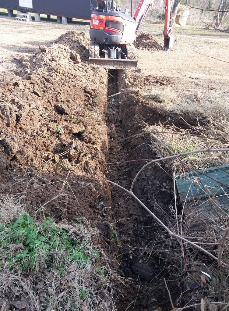 Excavator digging a trench beside a dirt mound and exposed ground utility line outdoors
