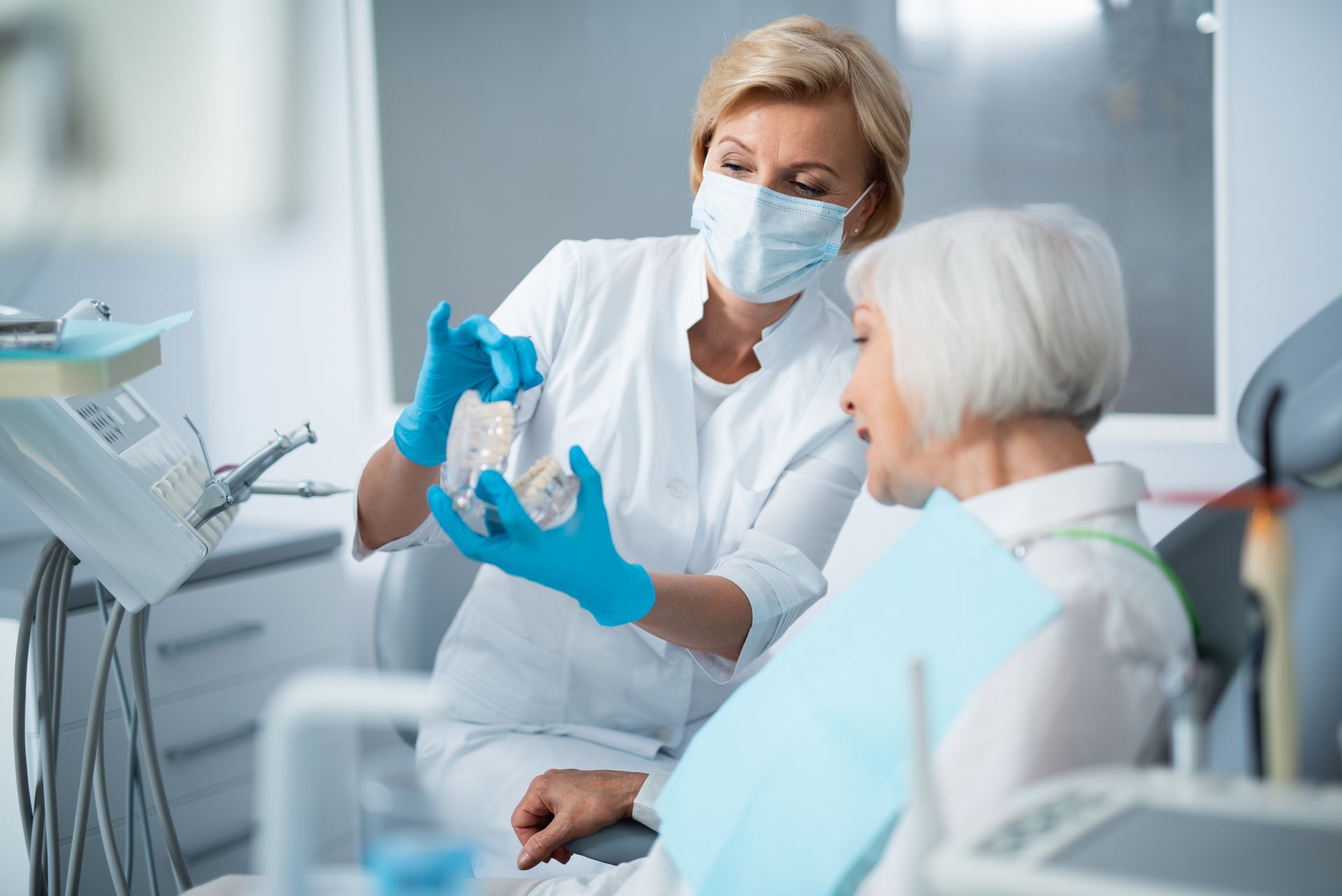 Dentist wearing mask and gloves examines elderly patient in a dental clinic