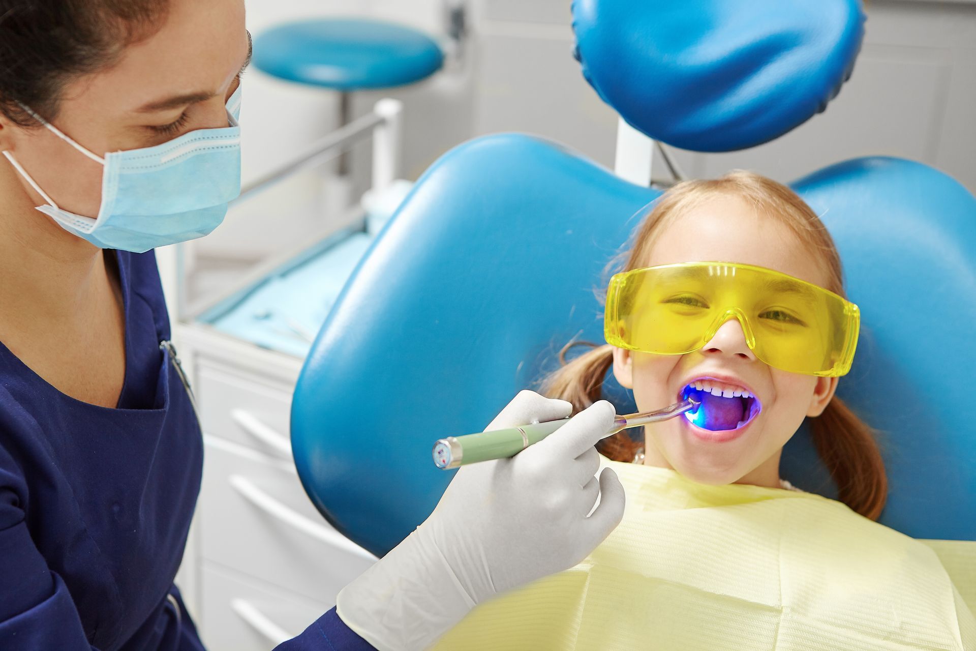 Dentist using a blue curing light on a patient wearing yellow safety glasses in a dental chair