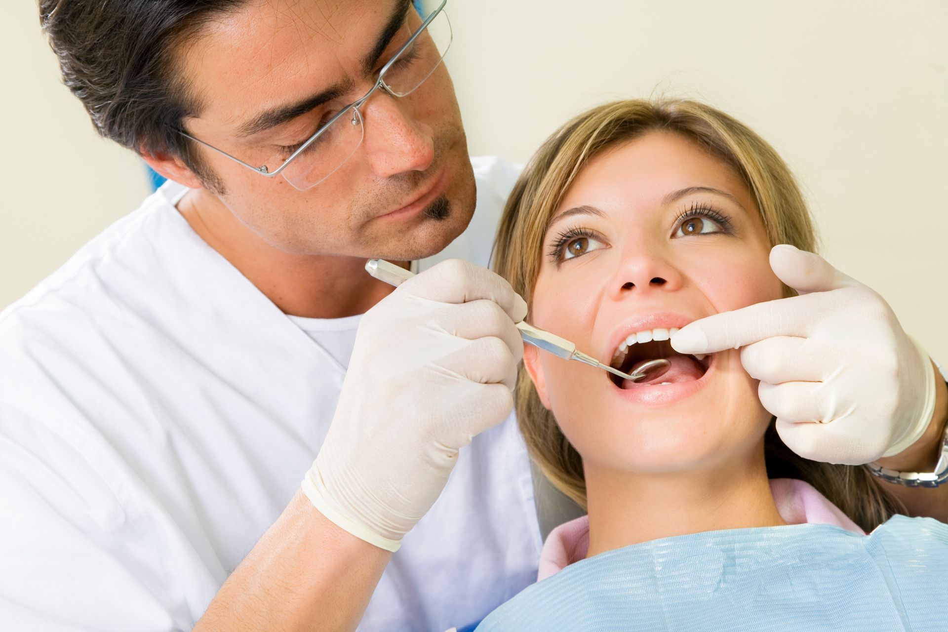 Dentist examining a patient’s open mouth with a dental mirror and gloves