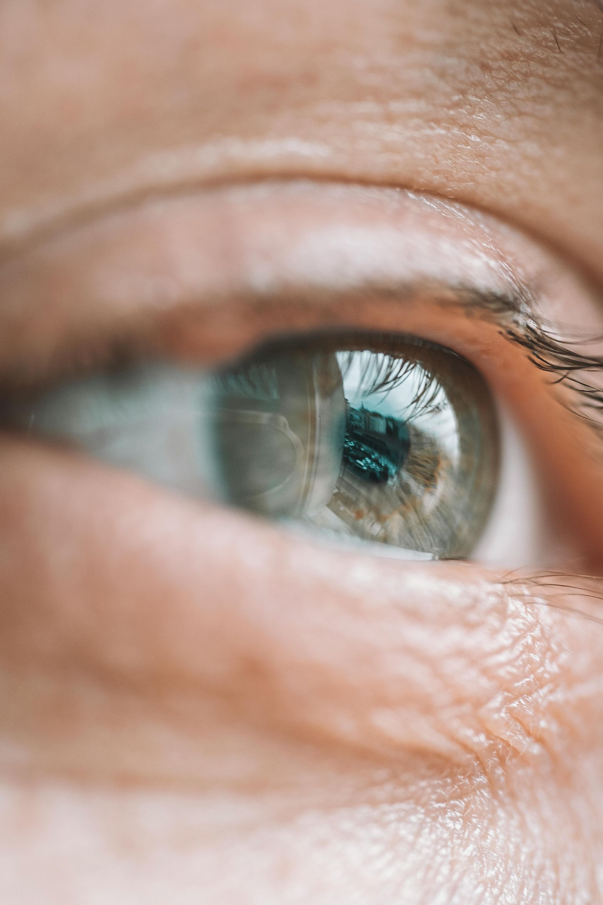Close-up van een blauwgroen oog met reflecties en een fijne huidtextuur eromheen.