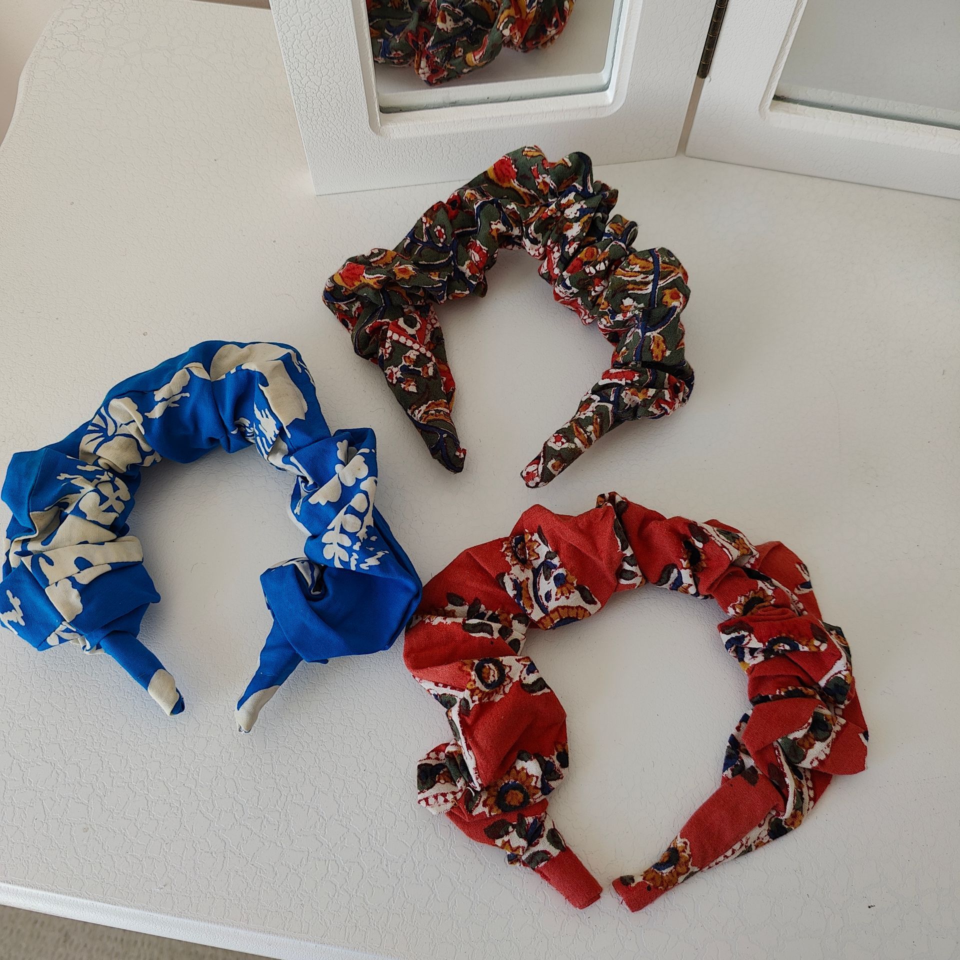 three floral fabric scrunchie 
headbands next to a mirror