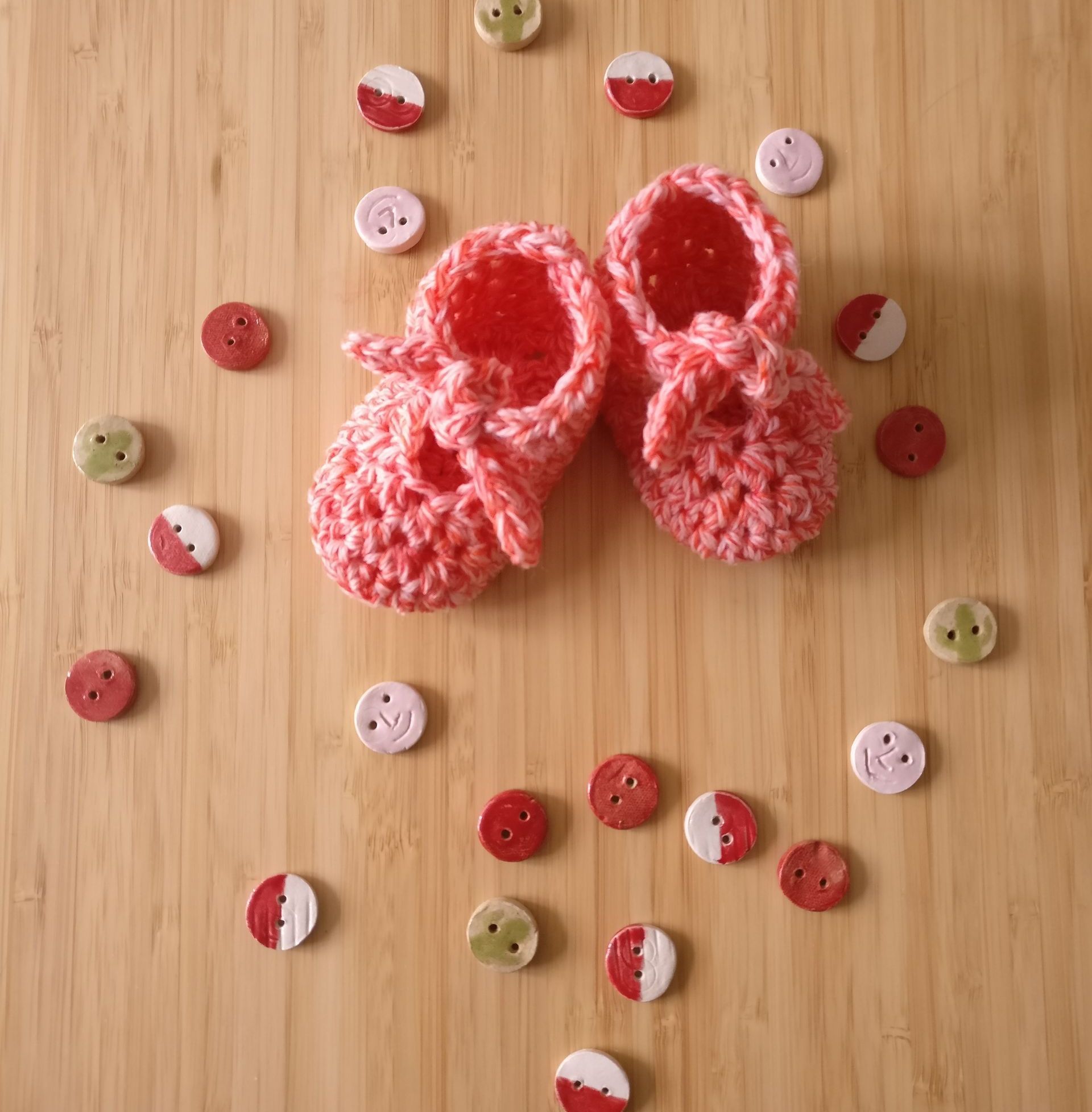 crochet baby booties in peachy pink surrounded by handmade ceramic buttons