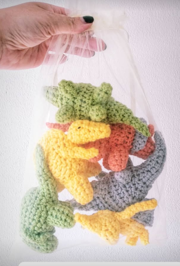 hand holding a see through bag of colourful crcohet dinosaurs