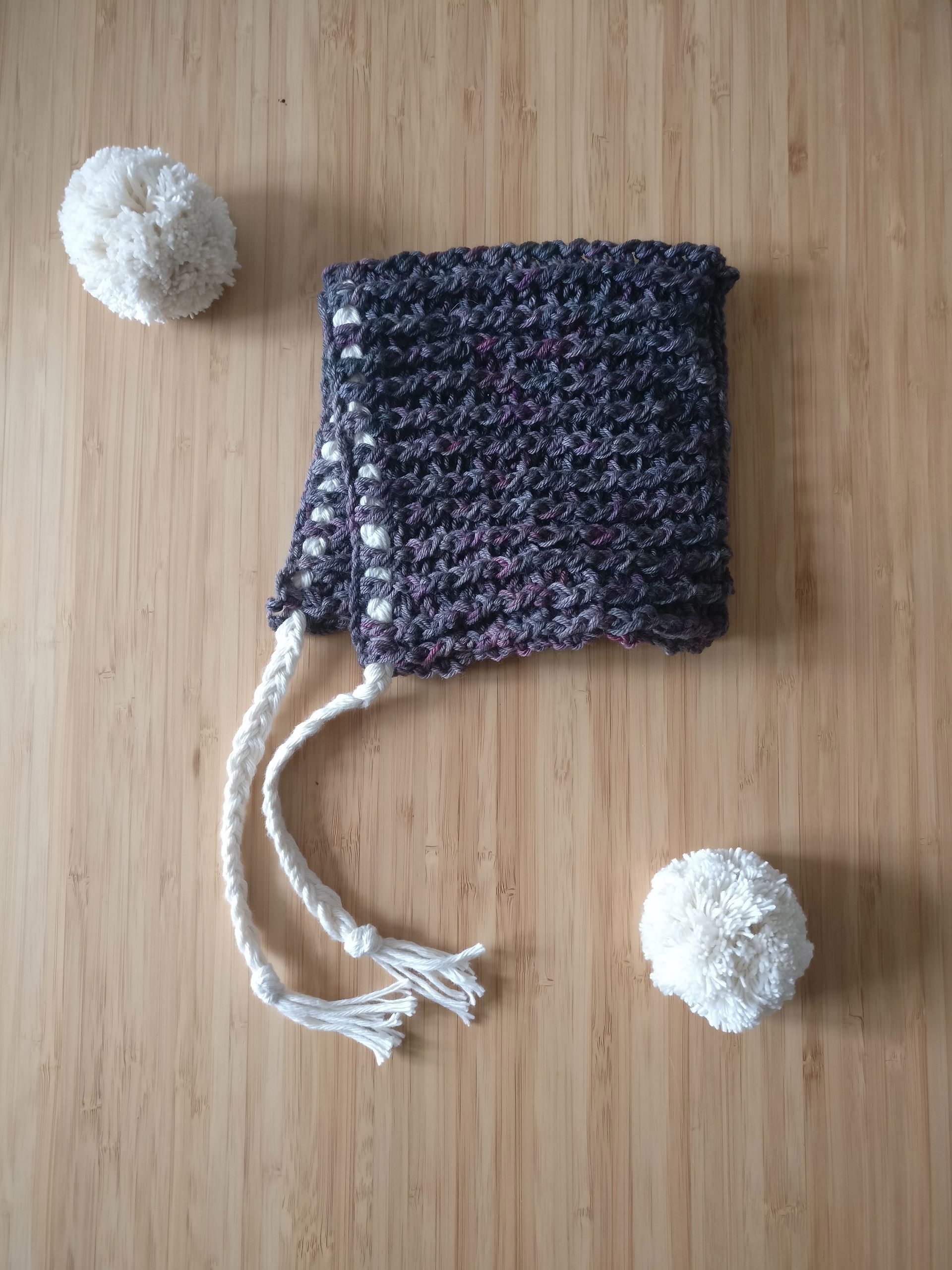 crochet baby pixie hat in grey with white pull and white pompom on a wooden surface