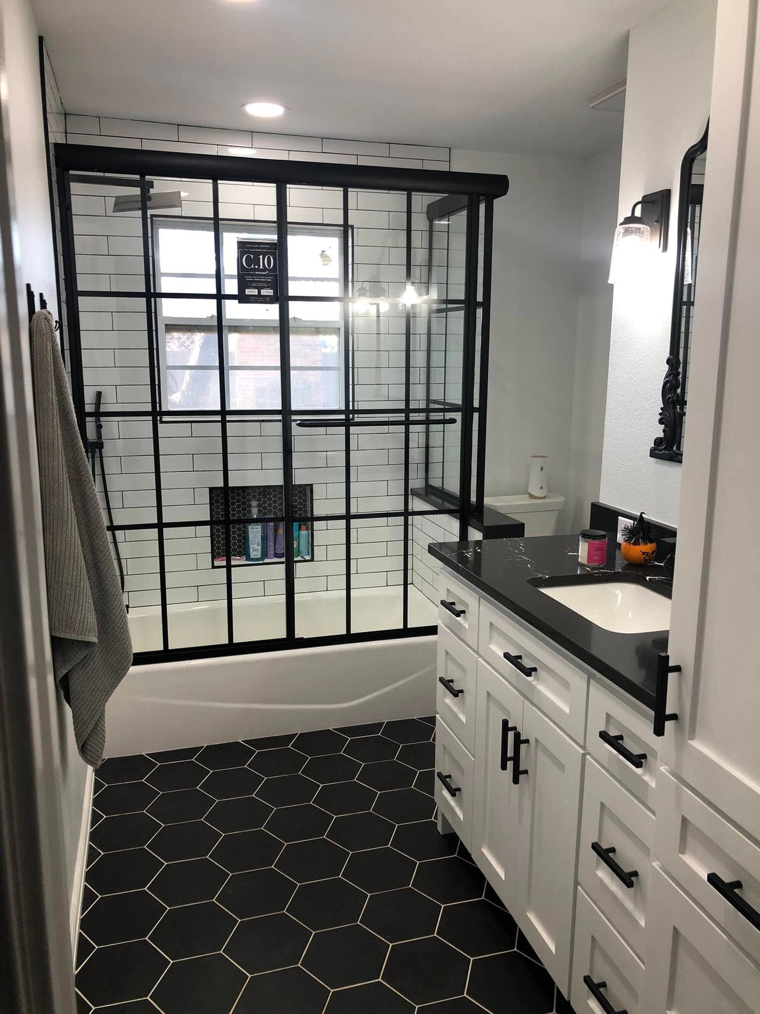 Modern bathroom with black and white tile. Black-framed shower and vanity. White cabinets, black countertops.
