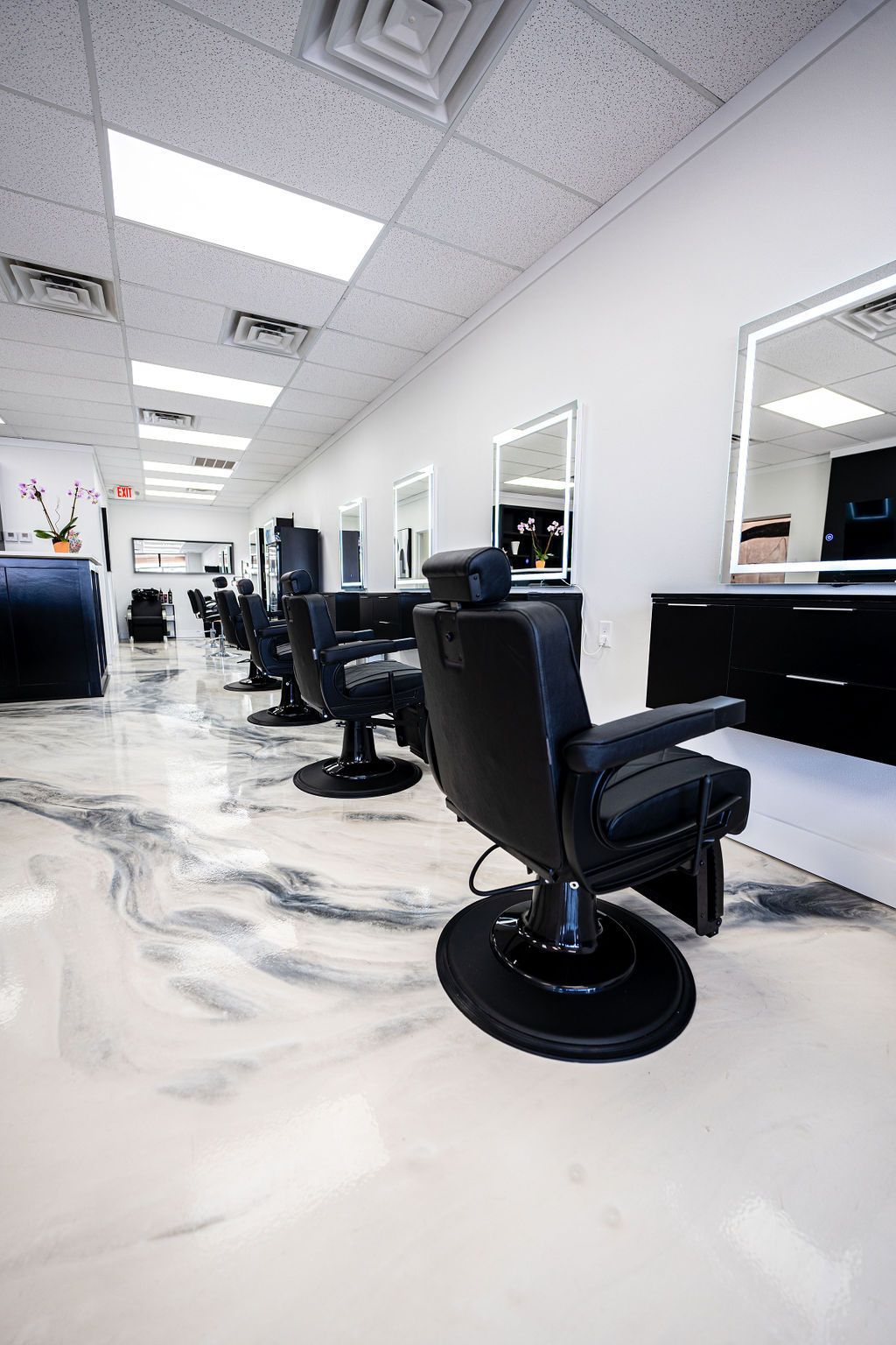 Hair salon interior with black chairs, mirrors, and marbled white and gray floor.