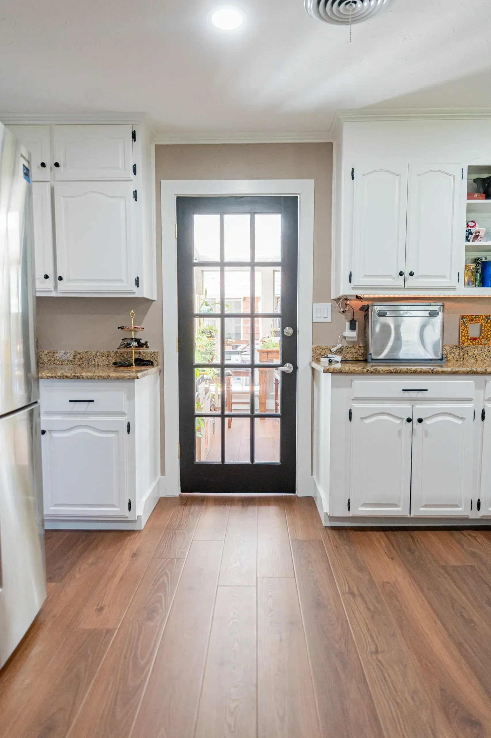 White kitchen cabinets, black glass door, and wooden floor.