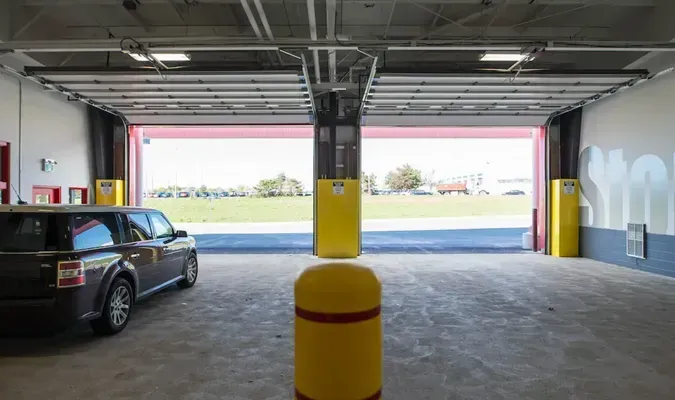 Car parked inside an open garage with a yellow pillar and a view of the grassy outdoors beyond.