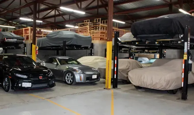 Cars in a garage, some on lifts and covered with car covers. Building interior with yellow markings and wooden structures.