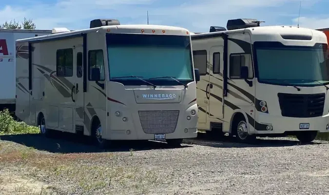 Two white recreational vehicles parked side by side on gravel under a clear blue sky.