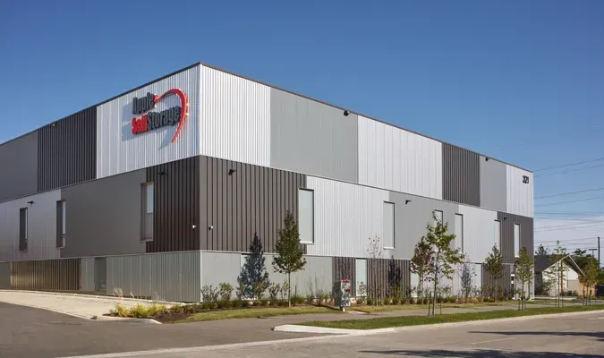 Modern industrial building with gray metal siding and a red logo on the corner, viewed from the street