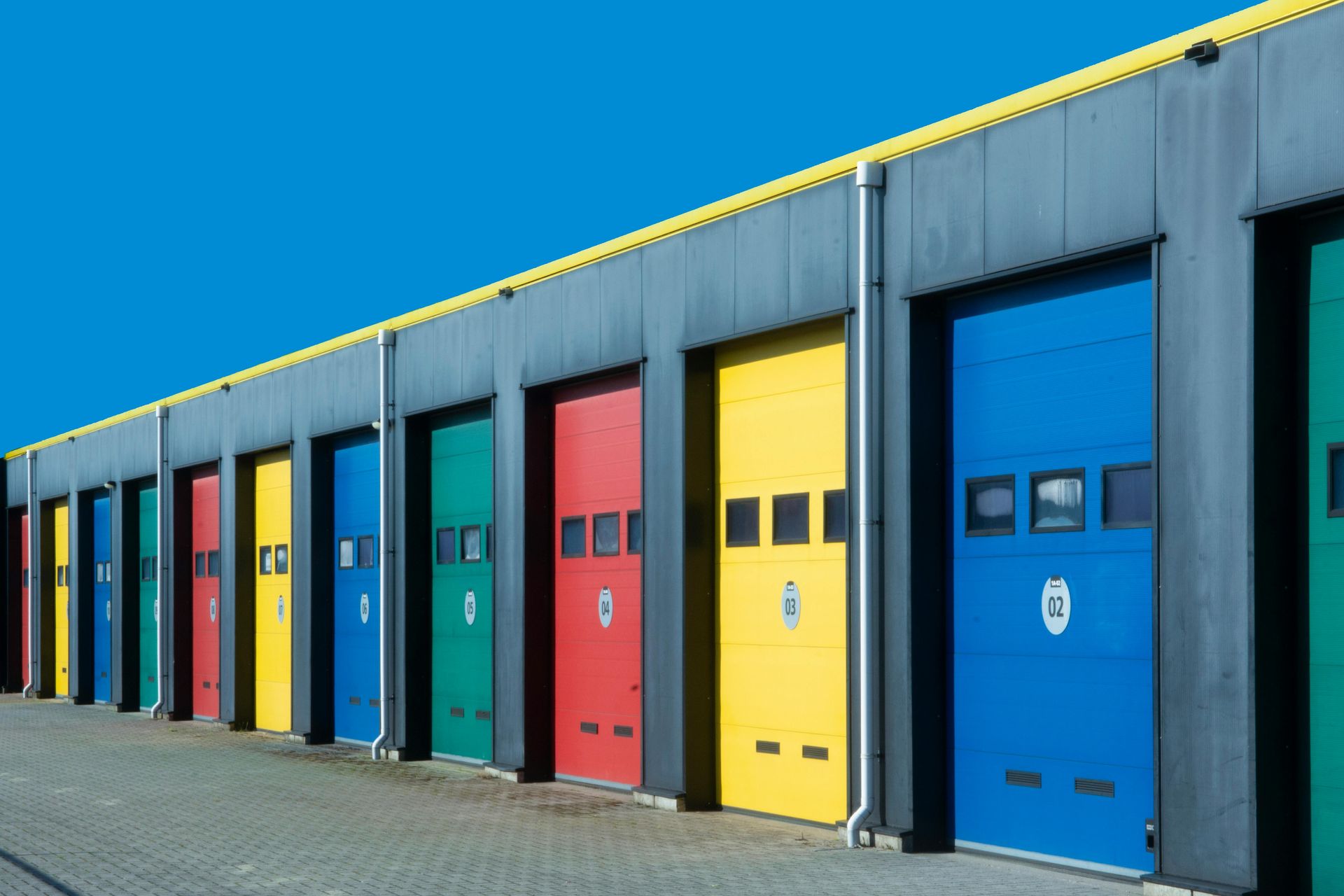 Row of colorful industrial garage doors on a metal building under a blue sky