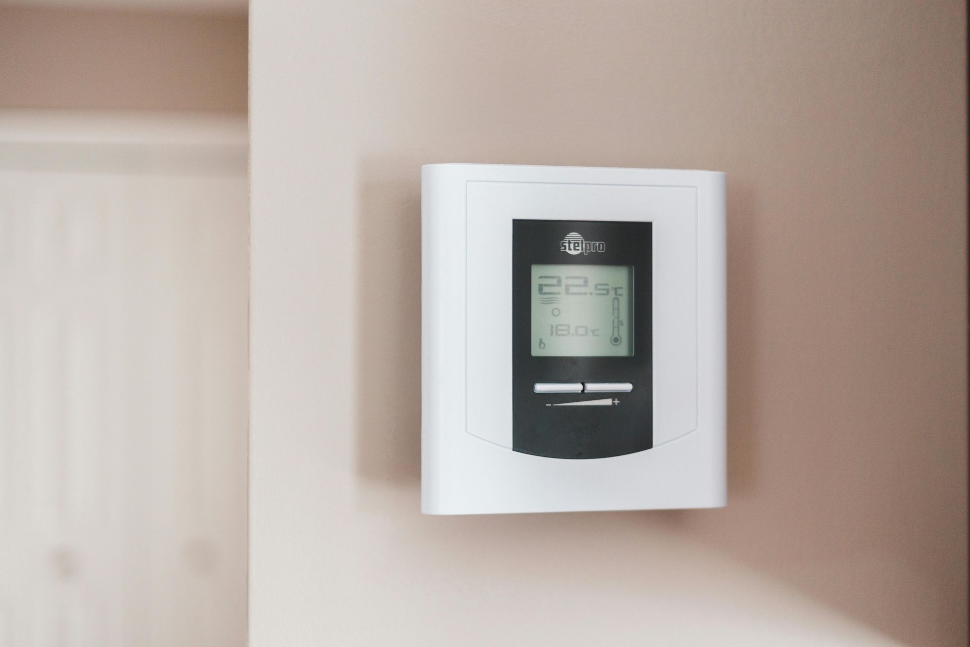 White wall-mounted thermostat with digital display on a beige wall near a doorway