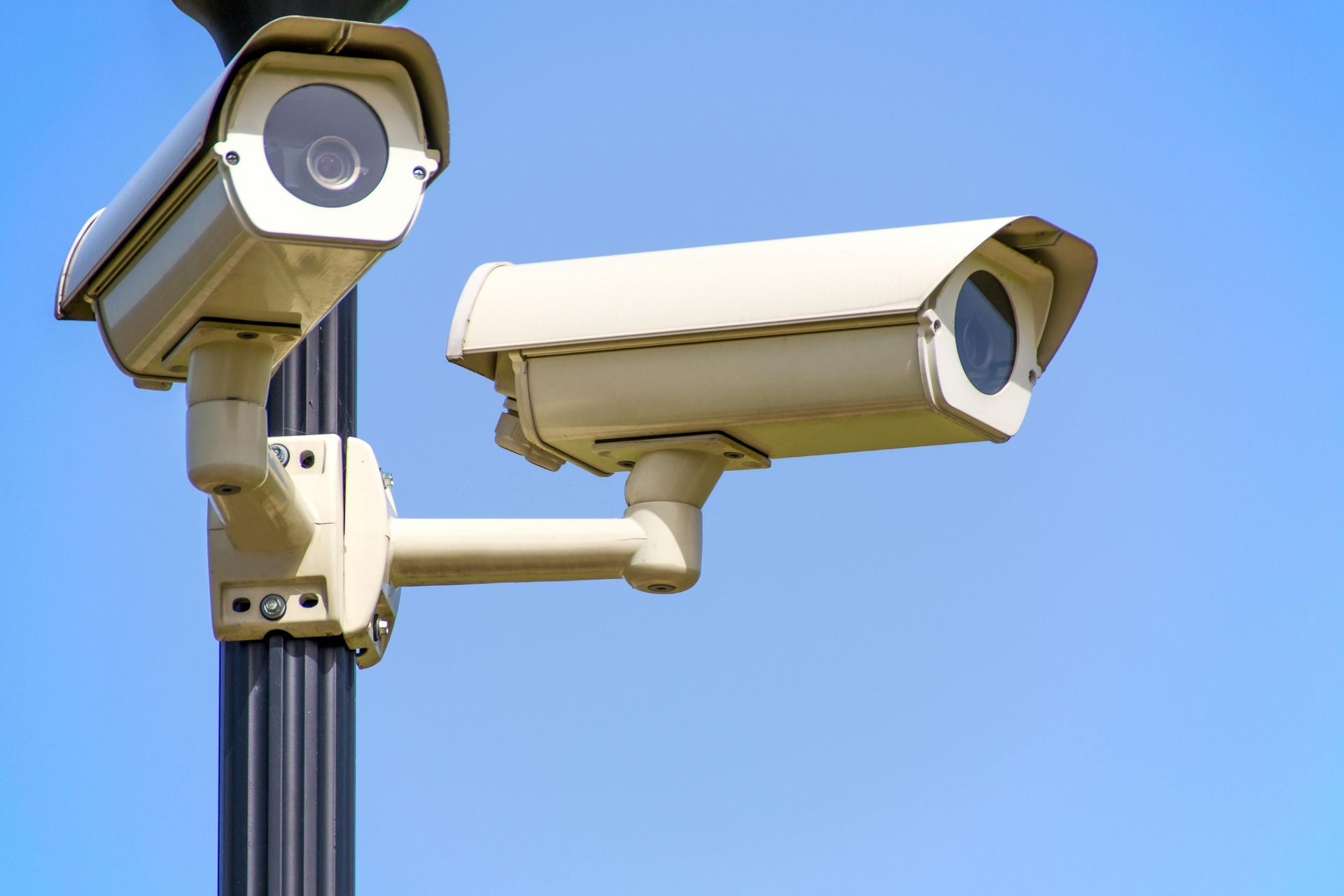 Two beige security cameras mounted on a pole against a clear blue sky