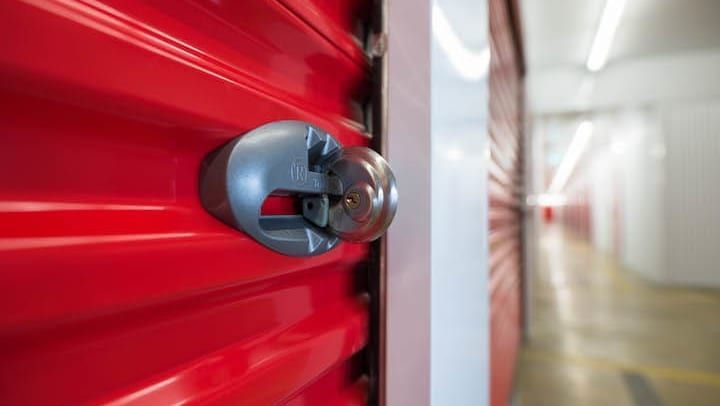 Close-up of a red storage unit door with a silver lock, in a hallway